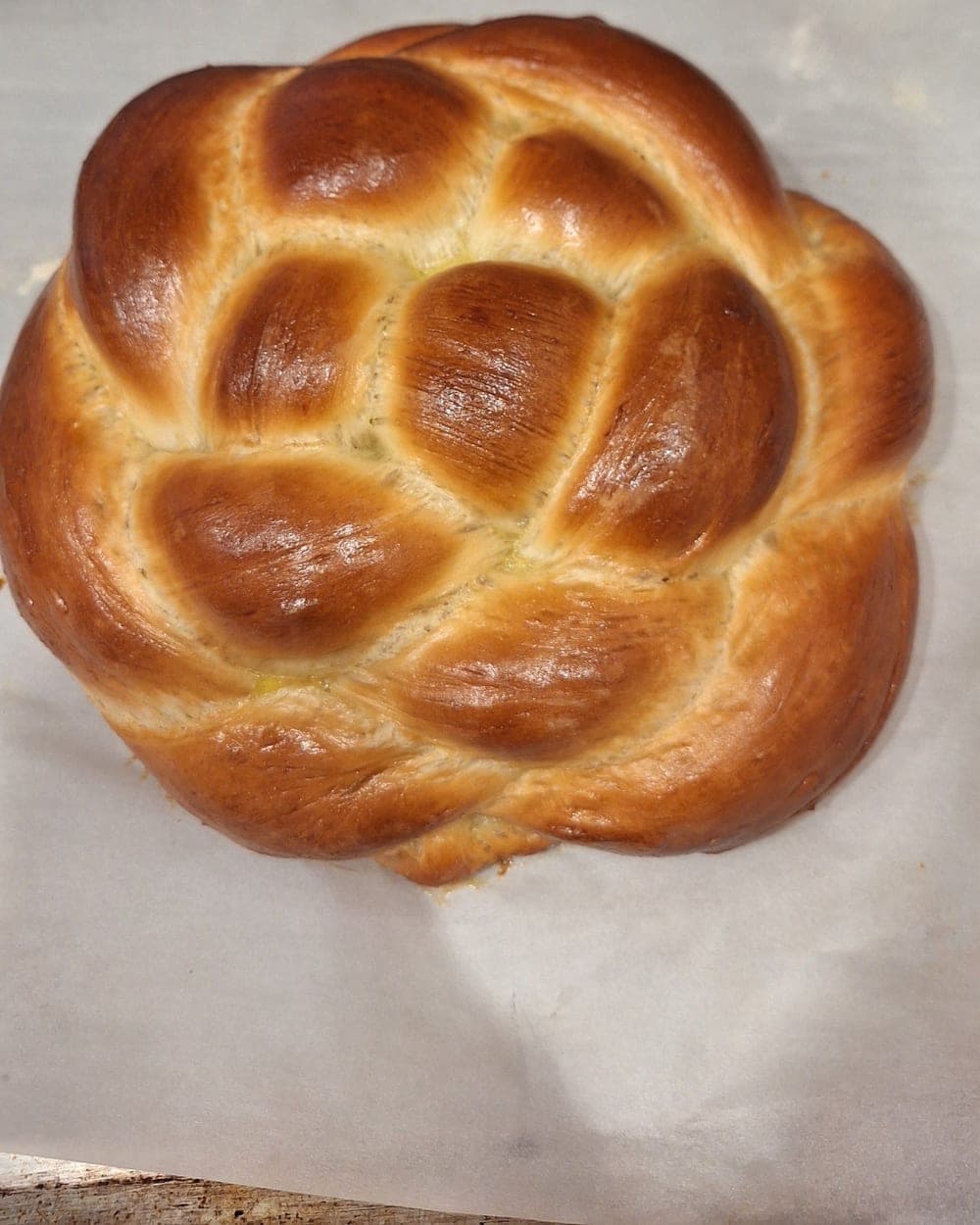 A round braided challah, freshly baked and cooling on parchment